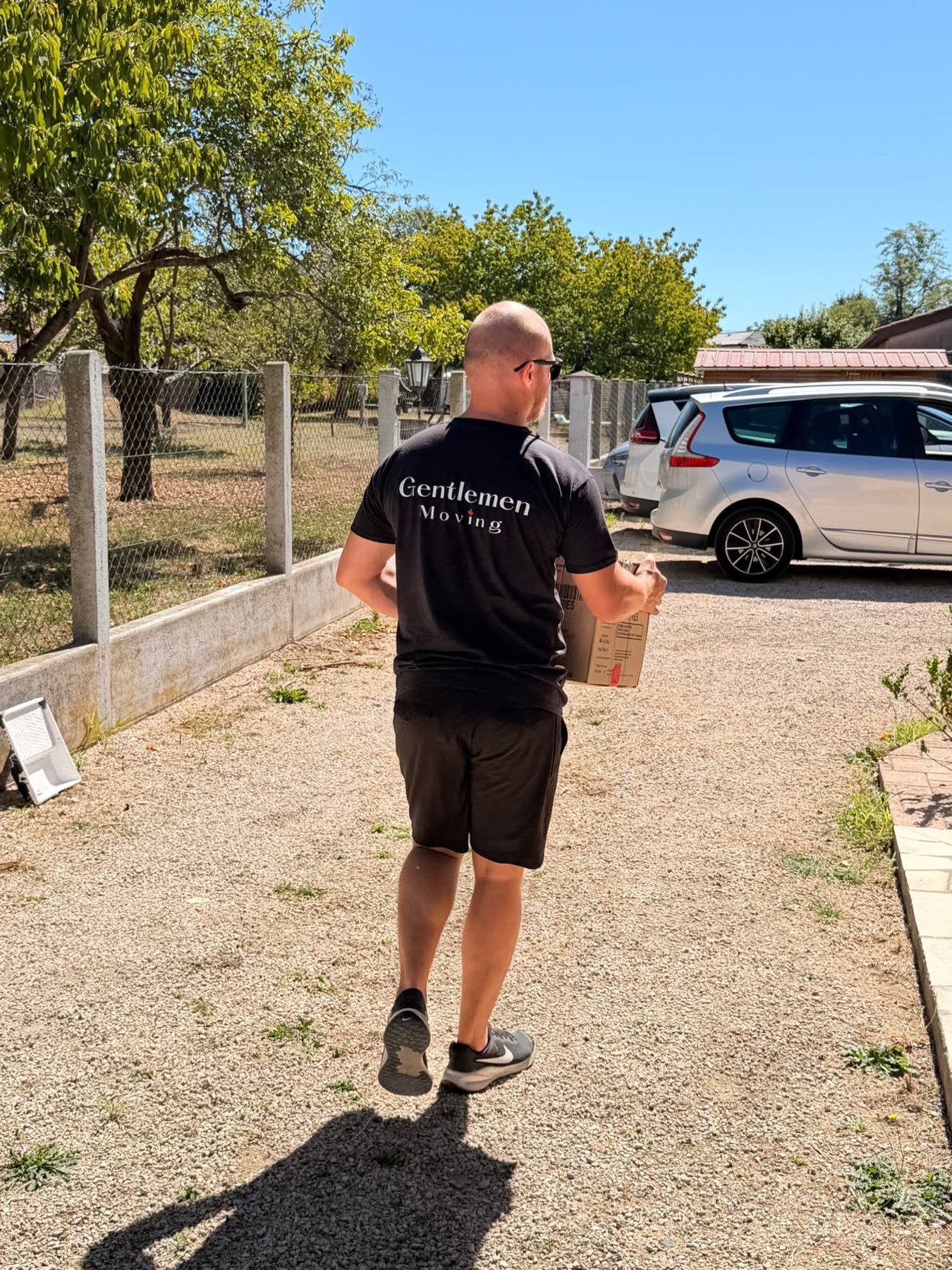 Déménageur en t-shirt Gentlemen Moving portant un carton dans l'allée d'une maison