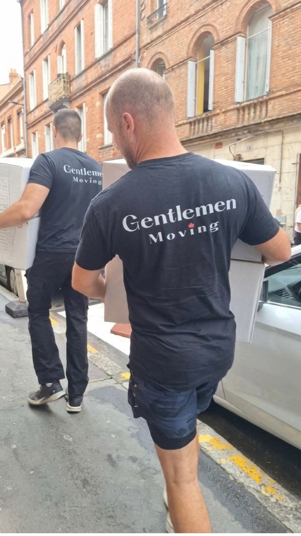 Deux déménageurs en t-shirt de l'entreprise portant un volume dans une rue